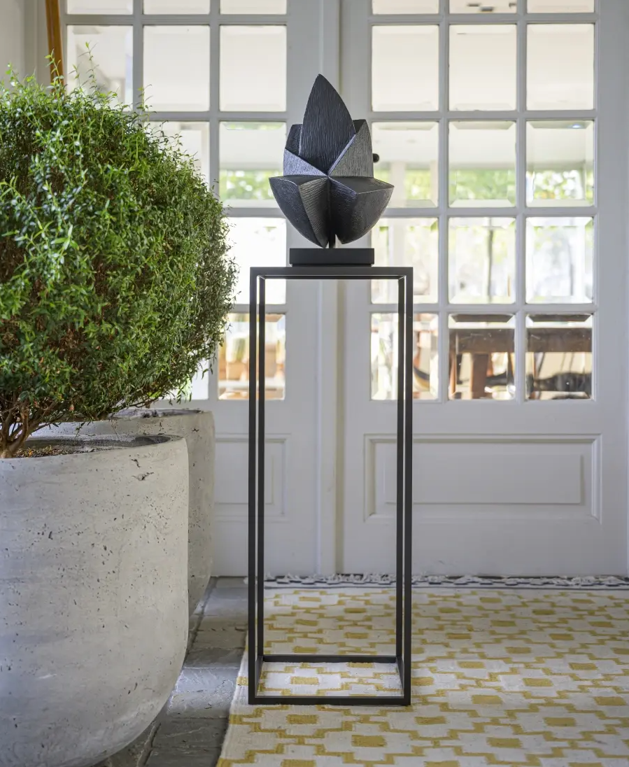 Decorative sculpture on a pedestal in a room with large windows and a plant.