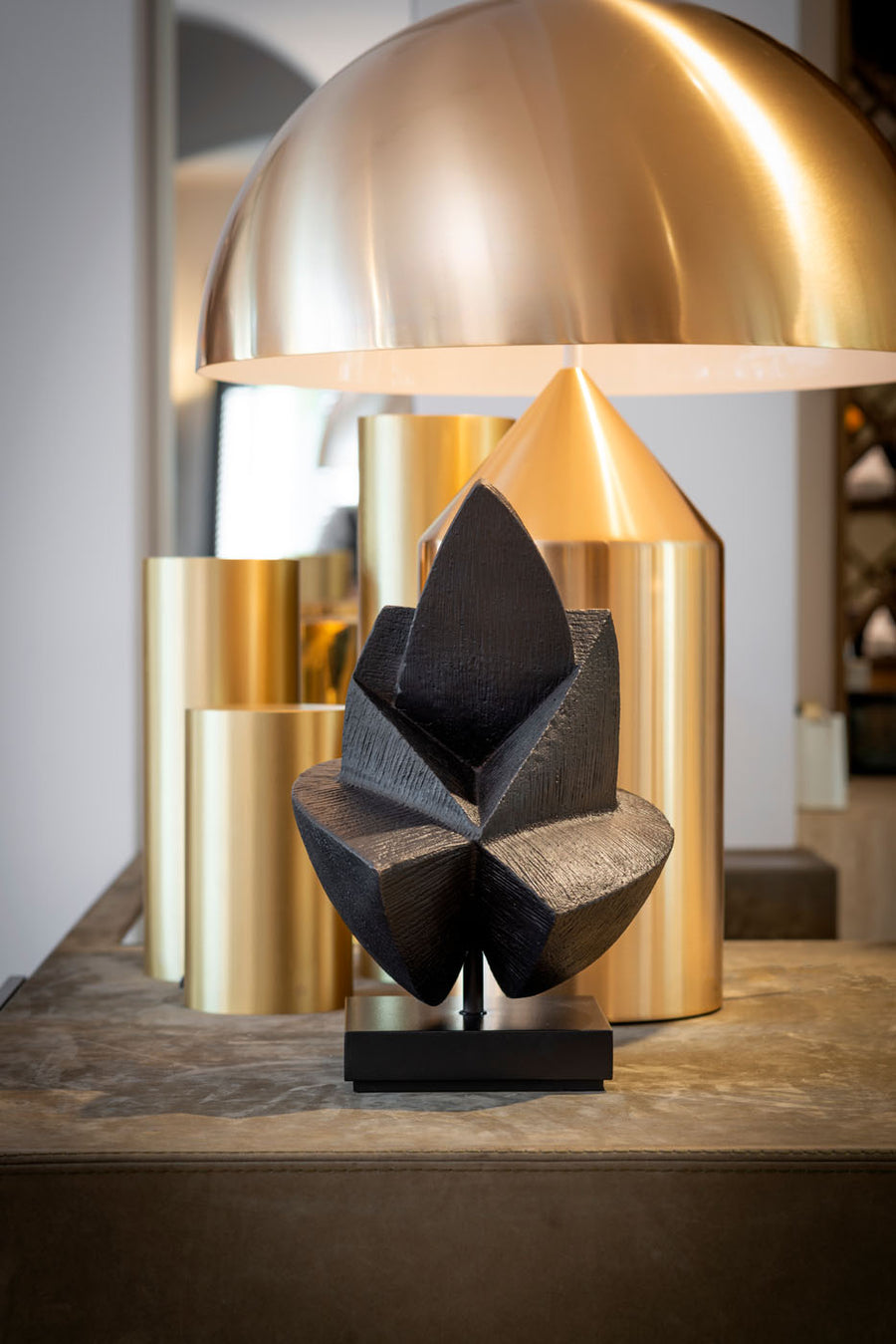 Decorative black sculpture on a wooden surface with gold lamp in the background
