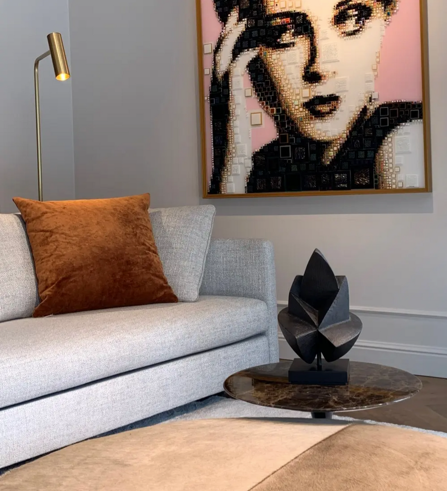 Living room with a gray sofa, brown pillow, and wall art of a woman's face and a black abstract bronze sculpture on a side table