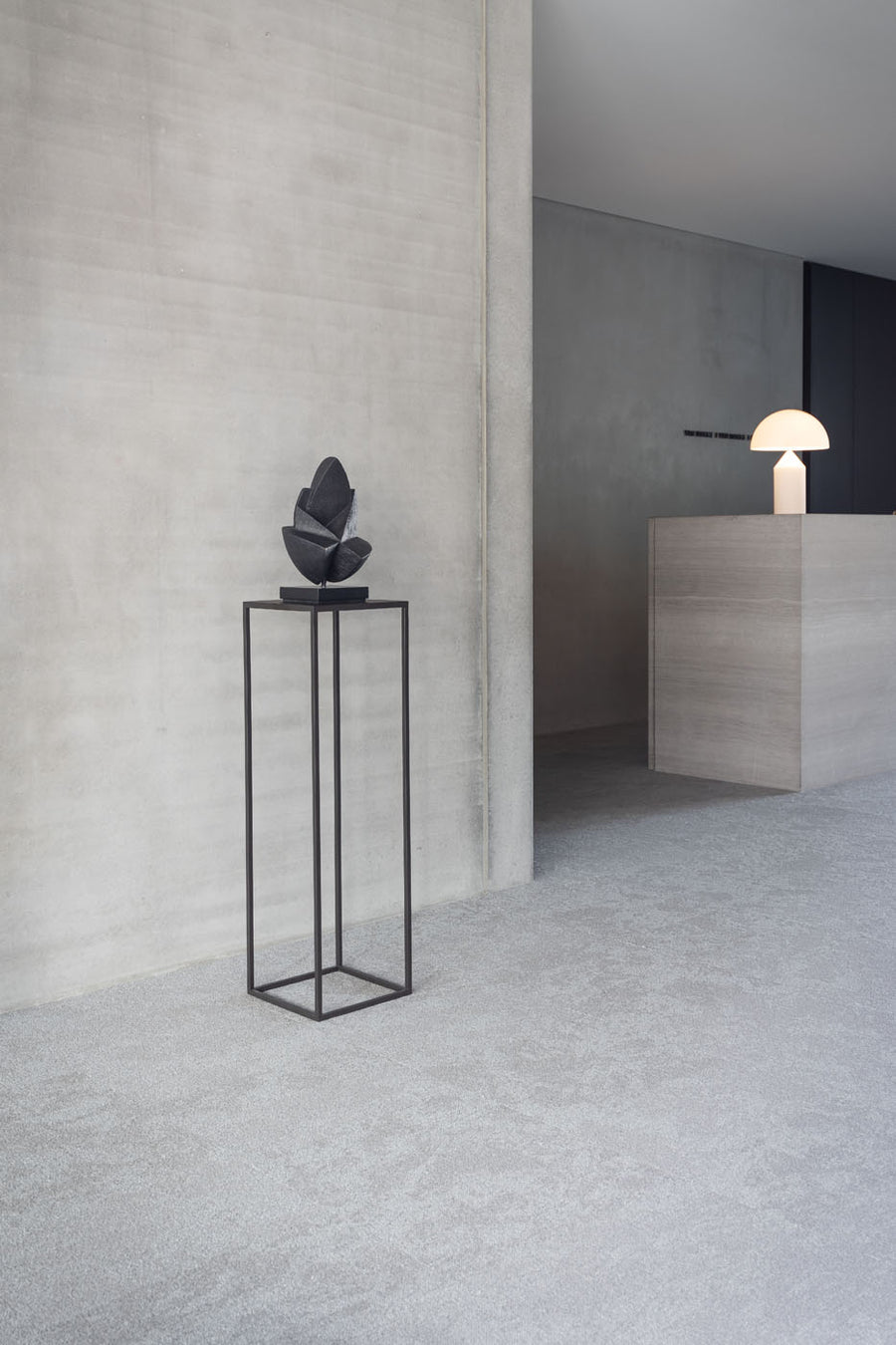 Modern interior with a black pedestal holding a decorative object against a gray wall.