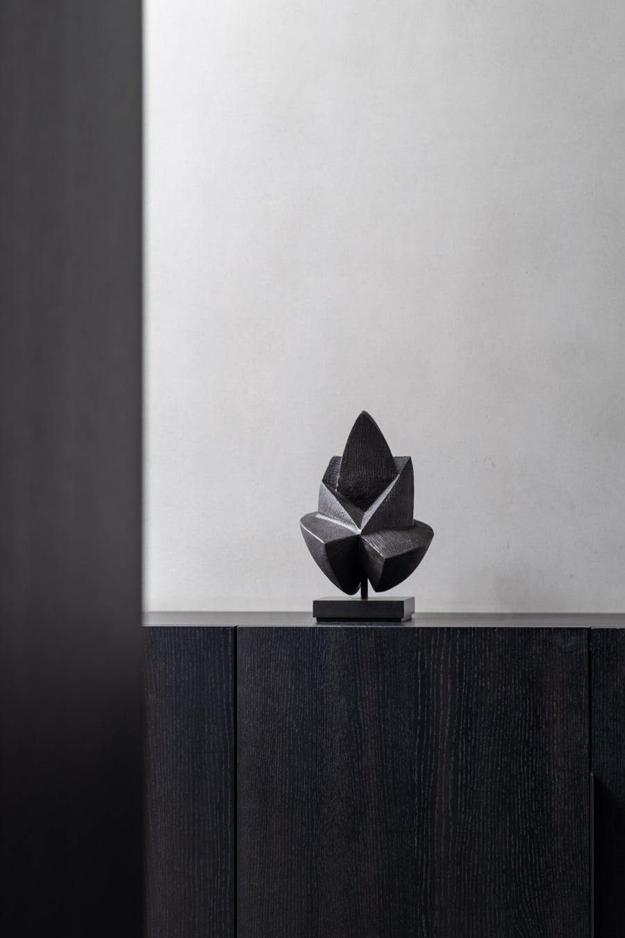 Black abstract sculpture on a dark wooden surface with a light gray wall background