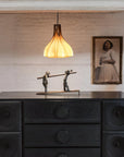 A bronze sculpture on a wooden sideboard below a yellow glass lamp and next to a lady portrait on a textured wall