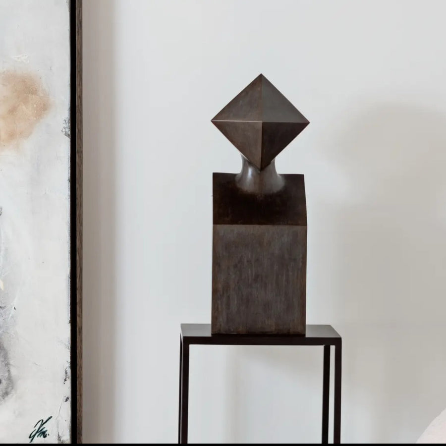Abstract bronze sculpture on a stand against a neutral background