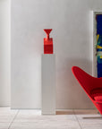 An elegant red chair sits next to a Gardeco Ceramic Sculpture The Muses Thalia Red on a white wall.