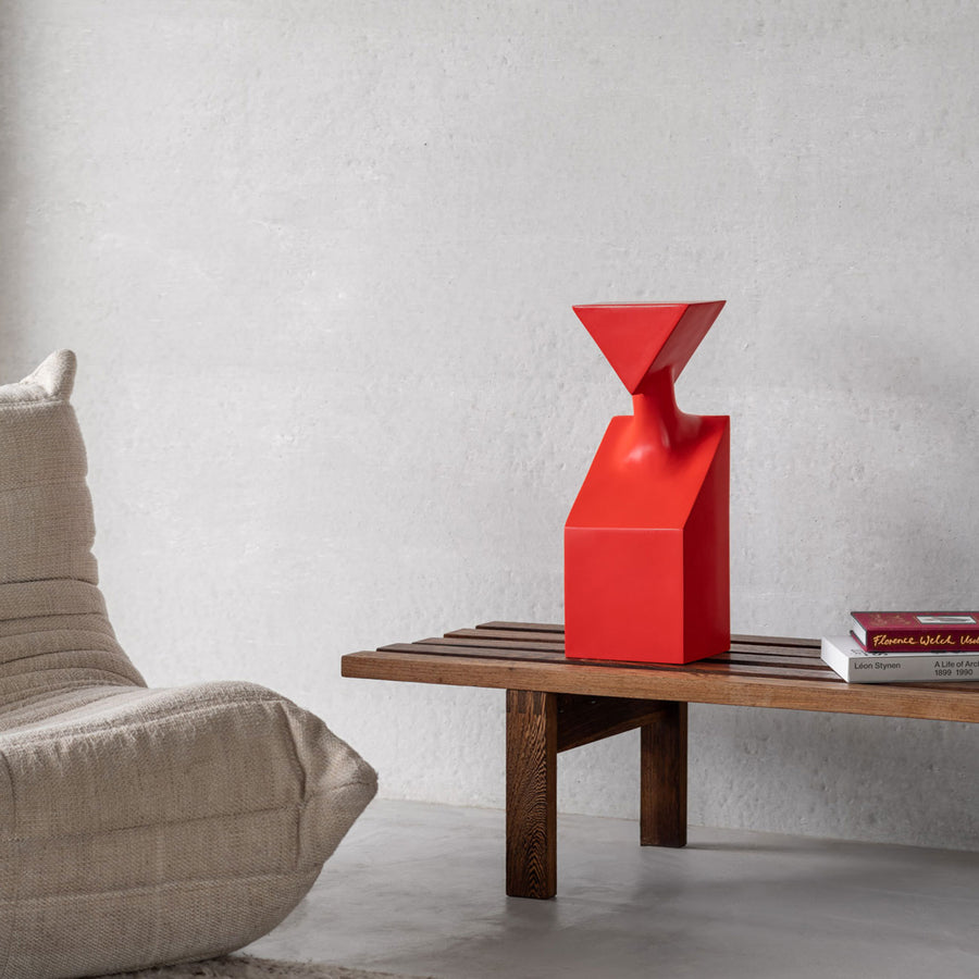 A Gardeco Ceramic Sculpture The Muses Thalia Red, a contemporary form of elegant sculpture, sits on top of a wooden bench.