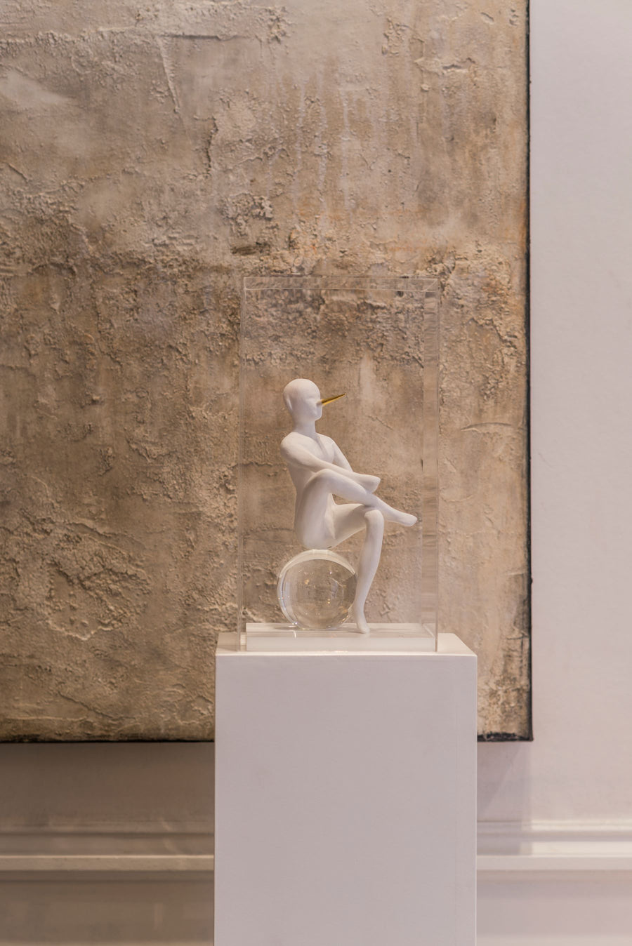 White ceramic sculpture on a pedestal against a textured wall.