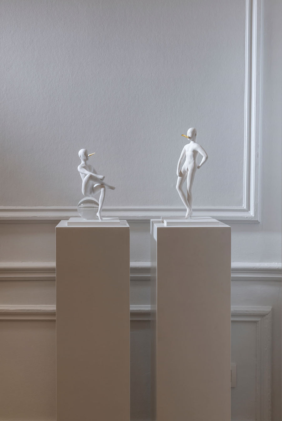 Two white sculptures - The Pinocchio & The Snob from Gardeco on pedestals against a plain wall