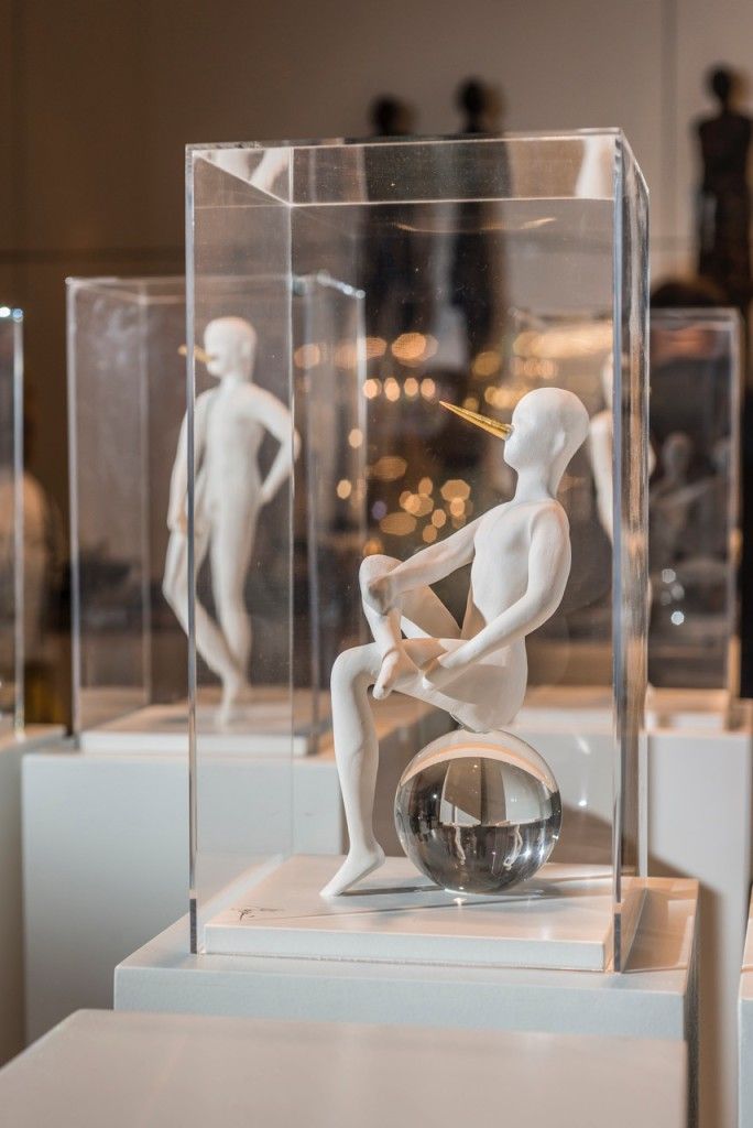 Sculpture of a seated figure with a glass ball inside, displayed in a clear case.