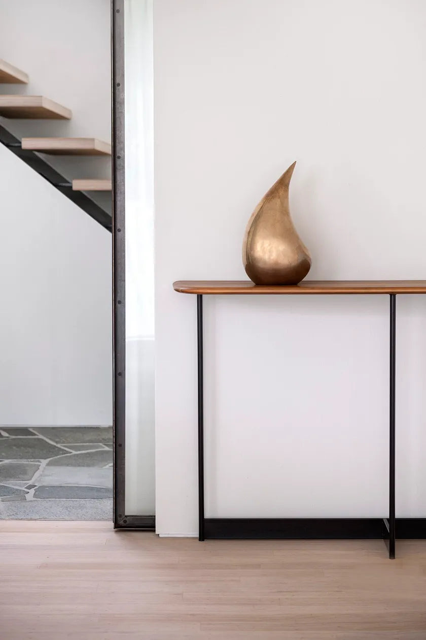 Modern interior with a gold sculpture on a wooden shelf next to a staircase.