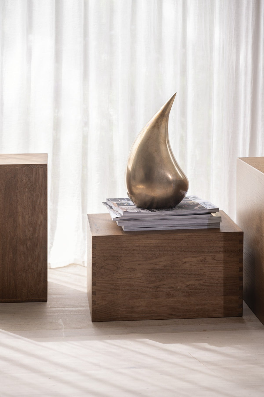 Bronze sculpture on a wooden pedestal with white curtains in the background