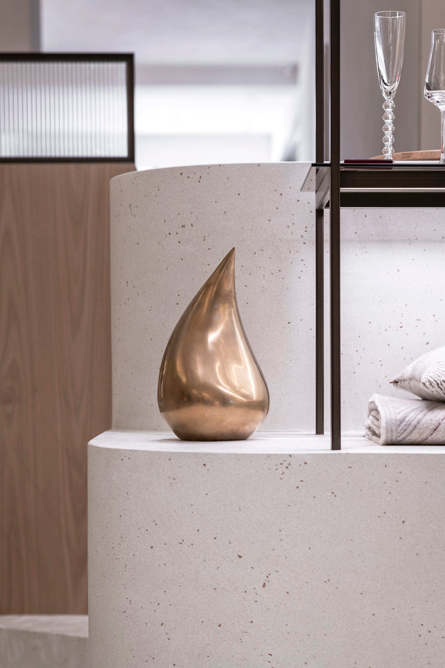 Bronze teardrop sculpture on a white surface with a blurred background