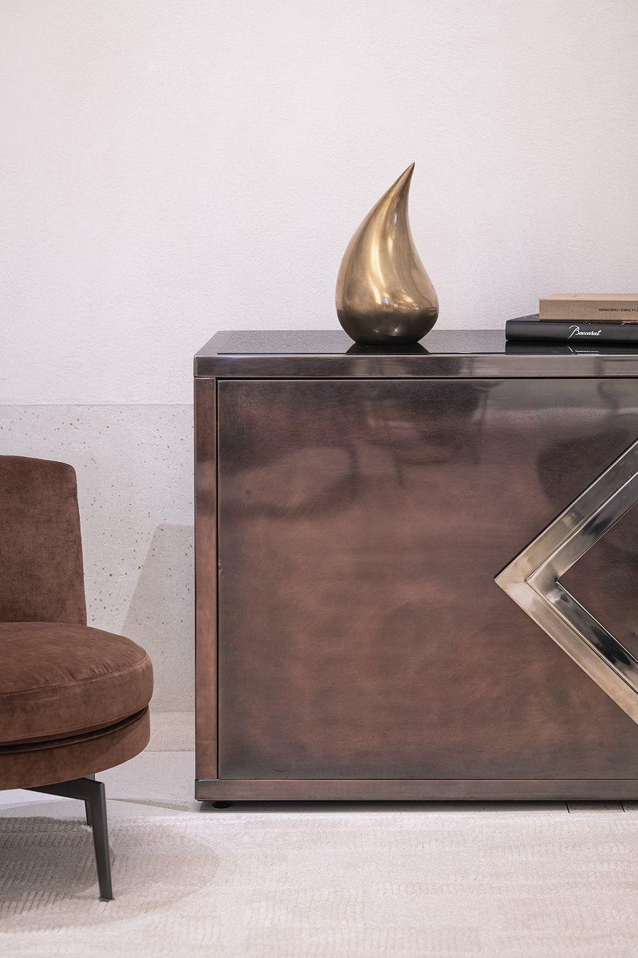 Bronze sculpture on a reflective surface with a chair and books in the background