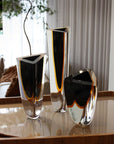 A collection of Gardeco Glass Vase Triangle 1 Black Amber vases displayed on a table.