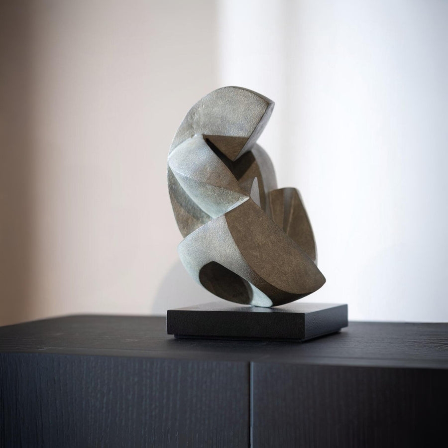 Abstract bronze sculpture on a black base against a neutral background