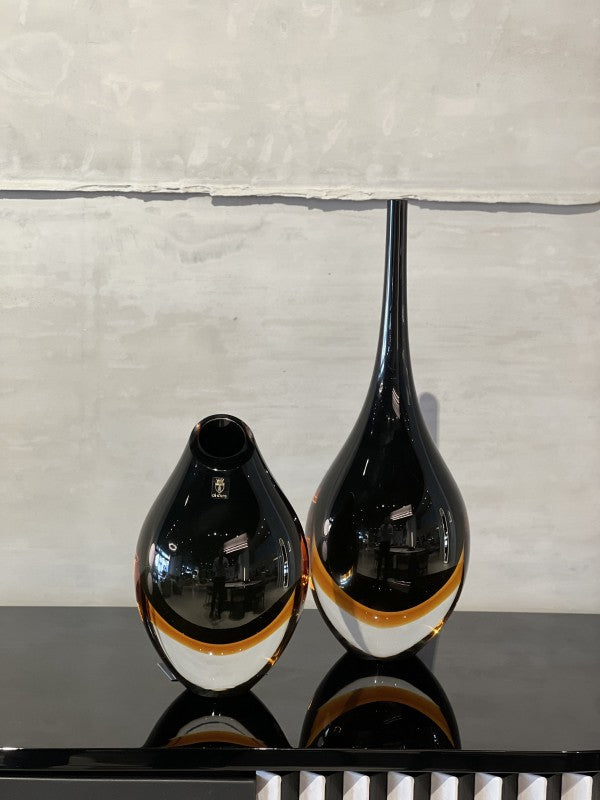 A Gardeco Glass Vase Drop Large Black Amber, with a hint of Black Fume Amber, sits elegantly on a table, adding sophistication to any decor.