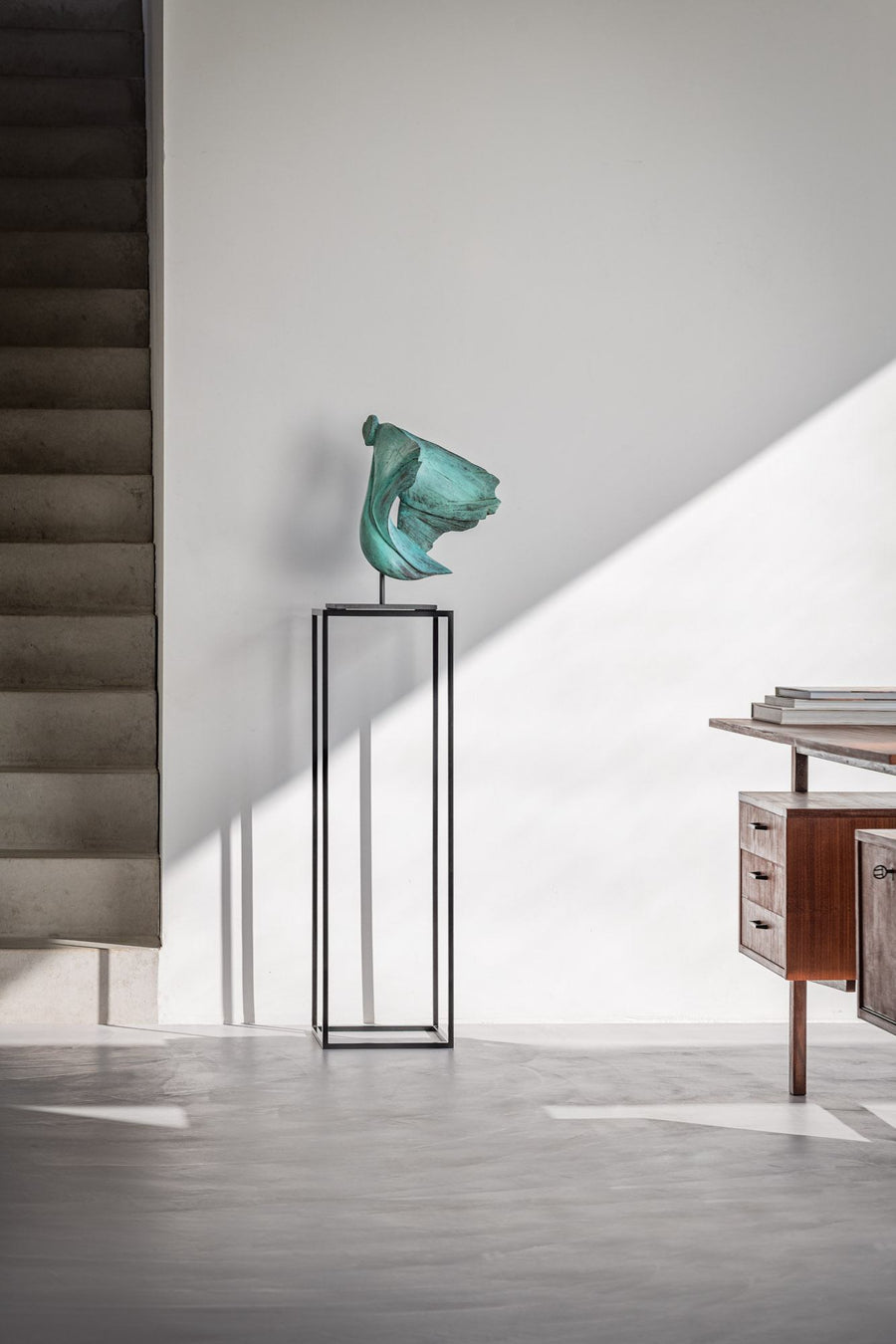 Modern interior with a green sculpture on a black stand and wooden furniture.