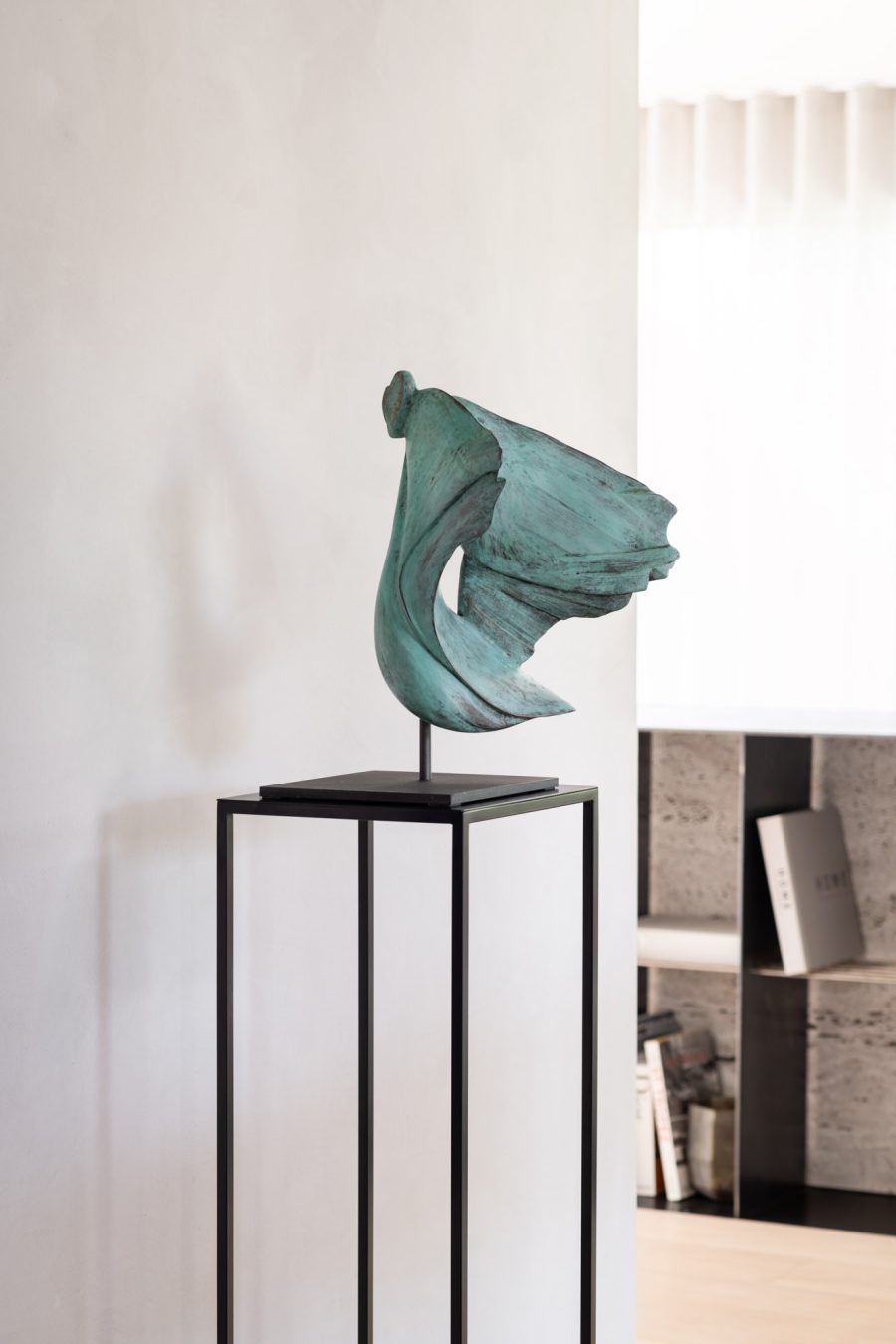 Green abstract sculpture on a black stand against a white wall