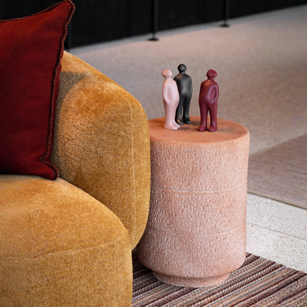 Round pink side table with decorative figurines next to a mustard yellow armchair with a red cushion.