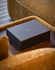 Black gift box with Gardeco brand logo on a wooden surface, surrounded by brown furniture.