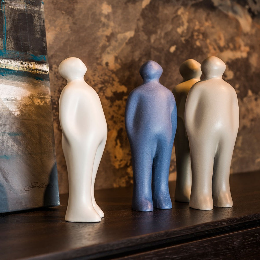 Four Gardeco Ceramic Sculpture Visitor Small Sand Cor02, selected by Guido Deleu, are delicately arranged on a shelf, adding a warm presence and enhancing the decor alongside a captivating painting.