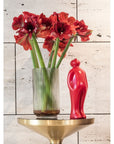 A Gardeco Ceramic Sculpture called "Visitor" featuring red daffodils in a vase on a gold table, showcasing the intersection of art and nature.