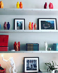 A shelf full of Gardeco Ceramic Sculpture Visitor Small Red Urucum figurines and art books.