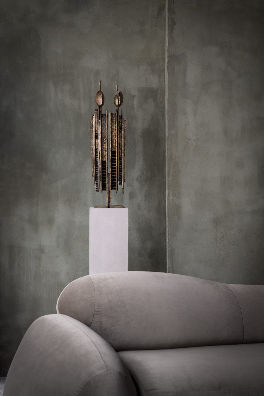 Decorative sculpture called Luxta from Gardeco on a pedestal in front of a textured wall with a gray sofa available at Spacio retail stores in India
