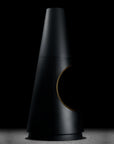A matte black cone-shaped modern lamp or decorative object with a circular cutout on the side, shown on a dark studio background with a small strip of warm gold visible at the cutout edge.