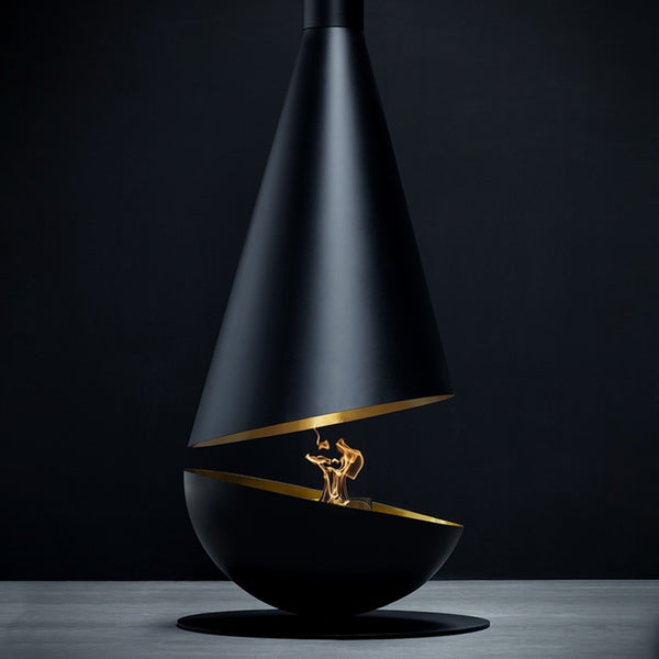 A modern black cone-shaped fireplace with gold interior accents and a visible flame, set on a dark studio background with a gray surface.
