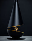 A modern black cone-shaped fireplace with gold interior accents and a visible flame, set on a dark studio background with a gray surface.