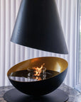 Modern black and gold fire pit with flames inside, set against a neutral background.