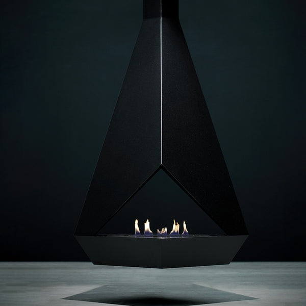 A modern black triangular indoor bioethanol fireplace with a glass wind guard and small flames burning inside, set against a dark charcoal background.