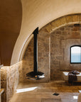 Bathroom with stone walls, a black freestanding bathtub, and a window overlooking water.