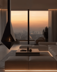 A modern living room with a large sectional sofa, low wooden coffee table, and a black suspended fireplace, set against floor-to-ceiling windows overlooking a city skyline at sunset.