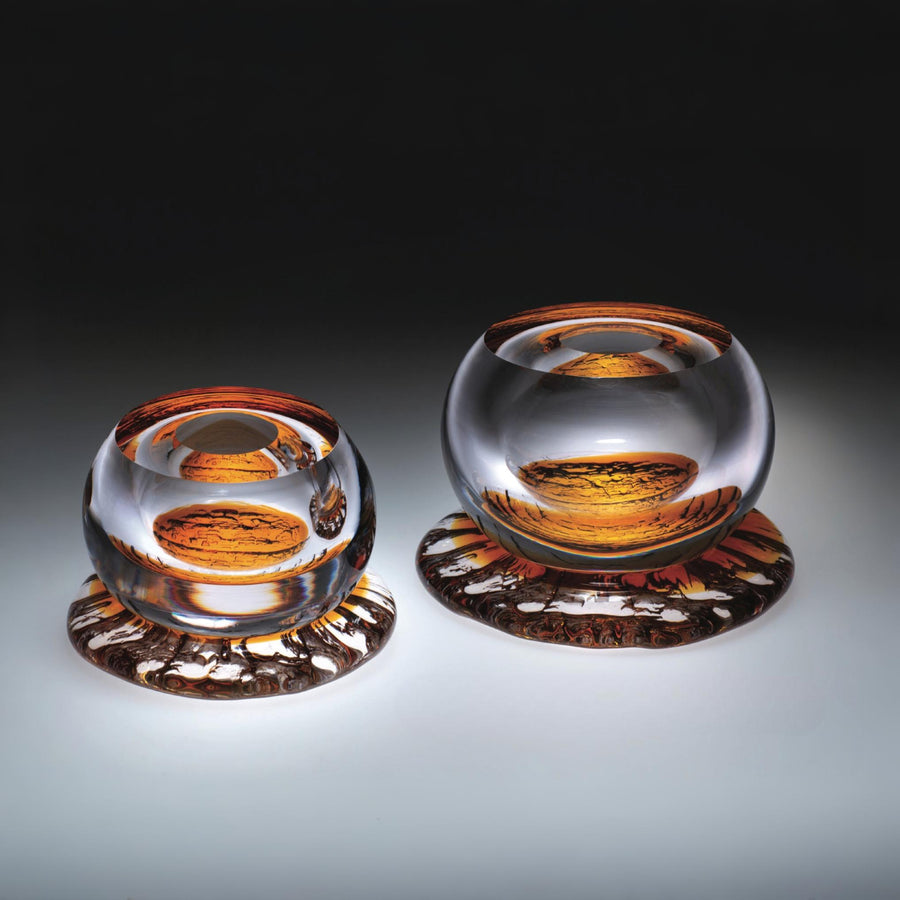 Two glass sculptures from Glasremis of Lithuania with amber-colored interior on a gradient background available at Spacio retail store in Mumbai. 