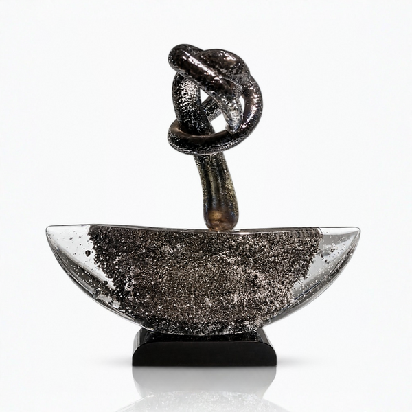 Decorative glass object with a knot design on a white background by Glass Remis available at Spacio in India. 