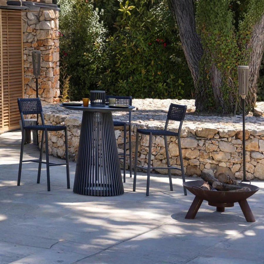 Outdoor patio setting with black chairs, table, and fire pit against a stone wall.