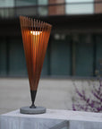 Tall, cone-shaped outdoor indoor solar lamp with wooden slats on a concrete surface.