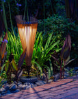 Tall garden solar light fixture in a garden setting with plants and a pathway.