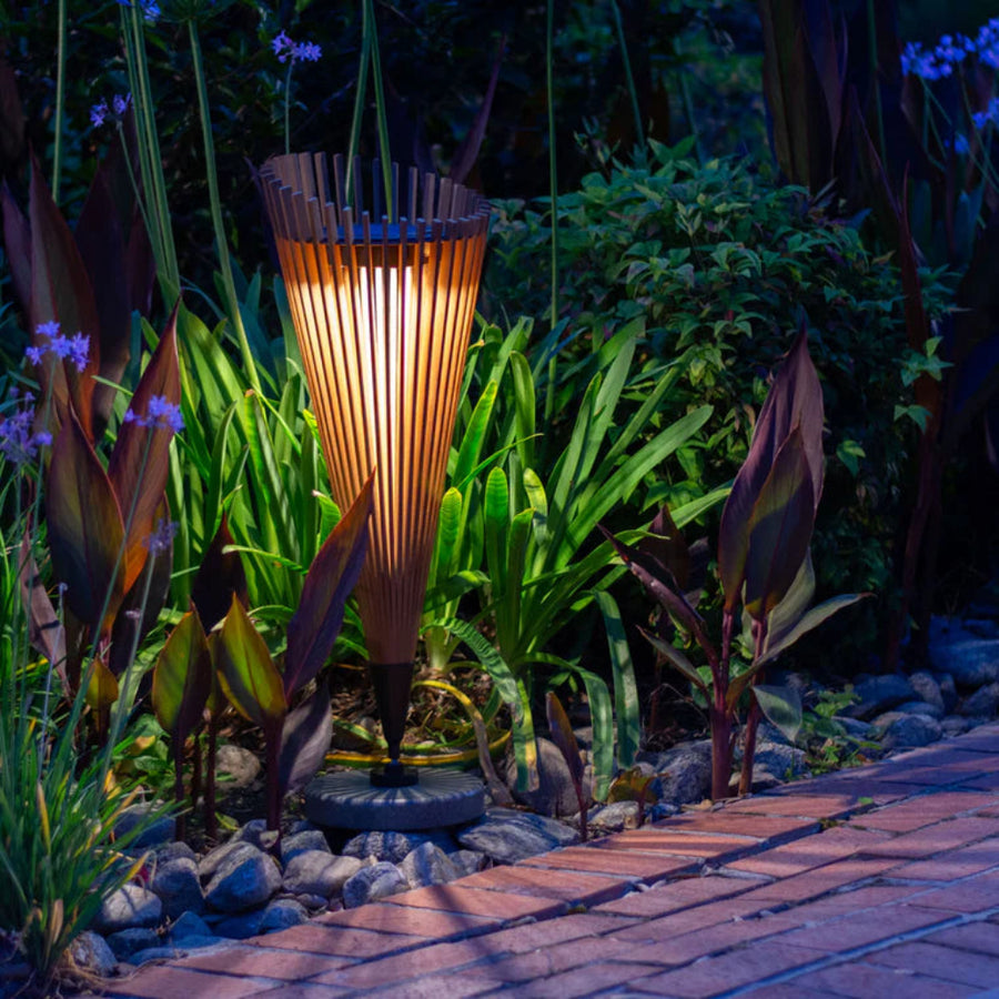 Tall garden solar light fixture in a garden setting with plants and a pathway.