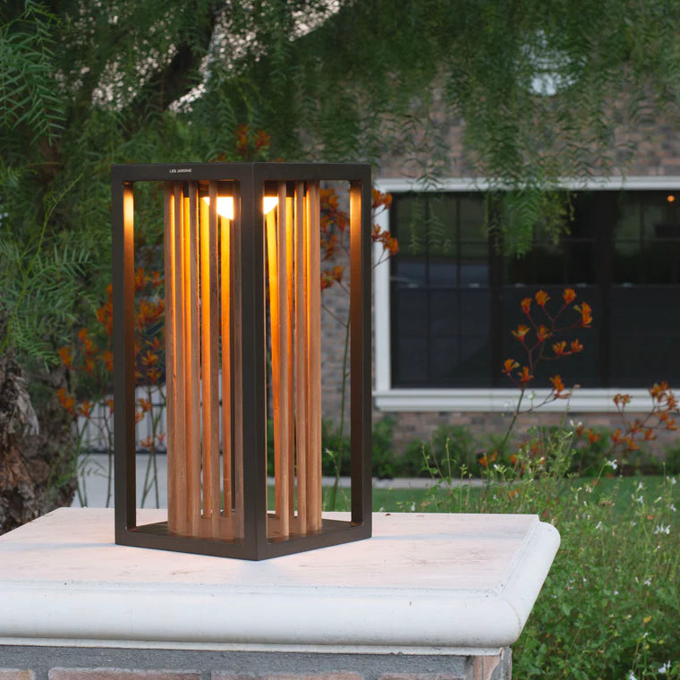 Decorative outdoor solar lantern with wooden slats on a stone ledge in a garden setting  by Les Jardins available at Spacio retail stores in Mumbai & Kolkata. 