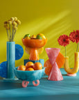 Jonathan Adler Mustique Orange & Yellow Bowl on blue surface with other collection of colorful bowls & vases available in India for Luxury Home Decor accessories collection of Tableware.
