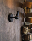 Black wall-mounted light fixture on a textured wall with a gold spiral sculpture in the background.