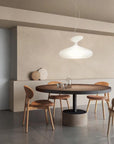 Dining area with a round wooden table and chairs under a modern pendant light.