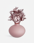 A sculptural object with a matte dusty pink rounded base and a highly textured, ruffled translucent pink glass top, set against a clean light gray background.
