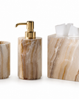 Three-piece bathroom vanity set made of beige and brown marbled stone, including a tissue box cover, a soap dispenser with a gold pump, and a tooth holder, on a white background.