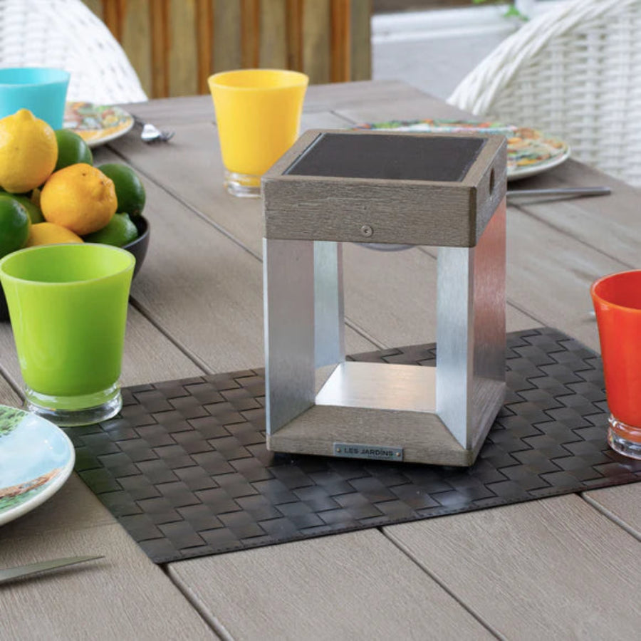 Outdoor table setting with a metal solar lantern, colorful glasses, and lemons on a wooden table.
