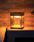 Solar lamp on a wooden surface with a warm glow against a stone wall.