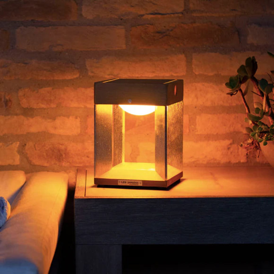 Solar lamp on a wooden surface with a warm glow against a stone wall.