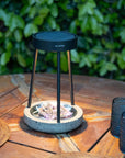 Outdoor solar table lamp with a black lid on a wooden table against a green bush background